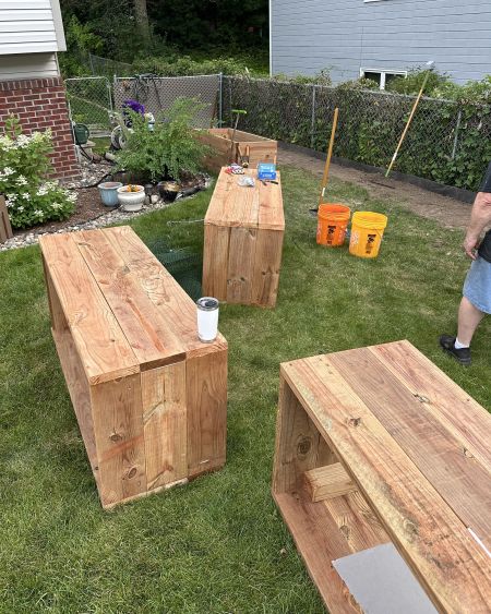 view of a front yard with 4 recently built raised garden beds lying on their sides near a fence being cleared for placement.