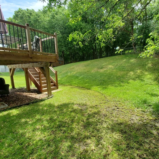 view of a grassy backyard with a steep hill leading down to a backyard deck with stairs.