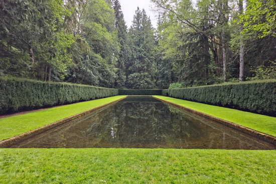 straight on view of a perfectly rectangular pond surrounded by cut grass and perfectly pruned evergreen hedges