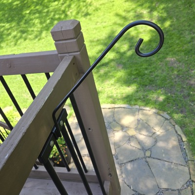 black swooping hook for a bird feeder, mounted to the side of a deck railing