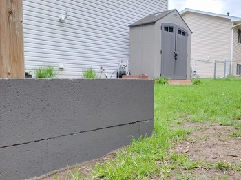 view of the side of a newly painted garden bed in a dark gray blue, with a garden shed framed in the background displaying the same color on the sheds doors.