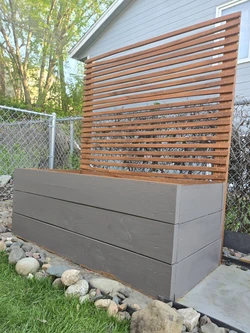 view of a raised garden bed built out of wood, but painted a dark blue gray color on the body, but stained an dark oak color on the attached back panel.