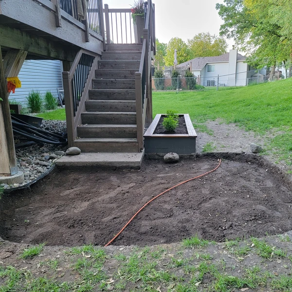 a backyard with a deck and stairs with dirt dug up for patio installation