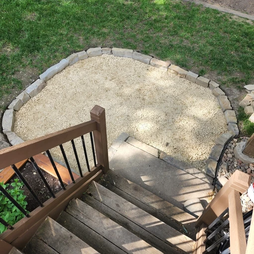 newly laid gravel inside of a dug out section of yard for patio installation, surrounded by flagstone edging.