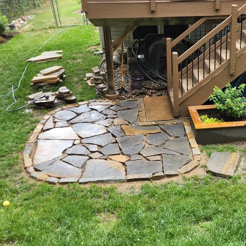 a finished flagstone patio with a stone walkway and a planter box on the side of a house