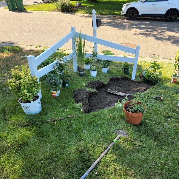 a yard with a white fence and flowers and shrubs being planted