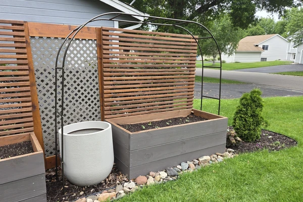 a view of a raised garden bed with a painted base and privacy panel attached to the back made of 1x4 wood slats.